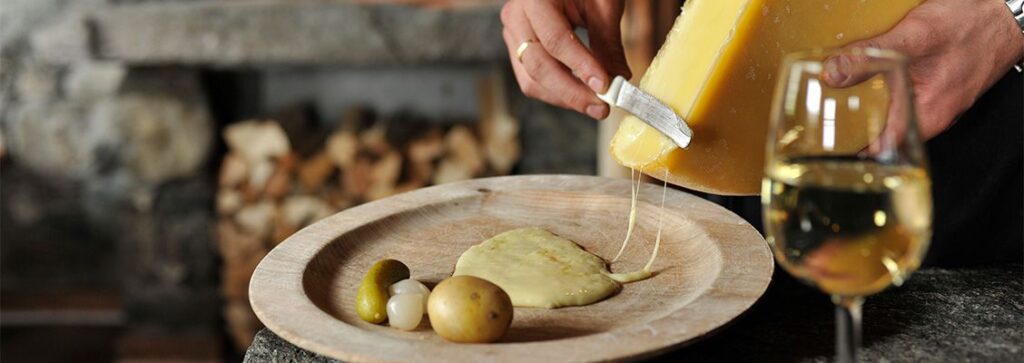A cheese raclette being scraped onto a plate