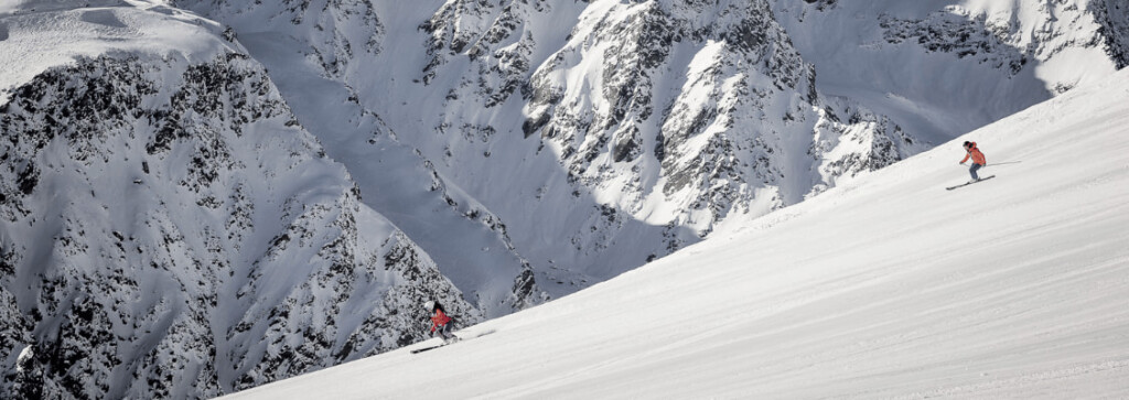 Two skiers carving down a freshly-groomed piste