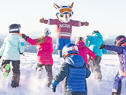 A group of children running towards a skiing mascot