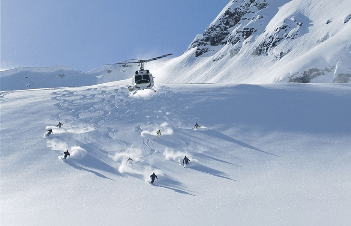 A panorama of skiers skiing through fresh powder snow with a helicopter flying above them